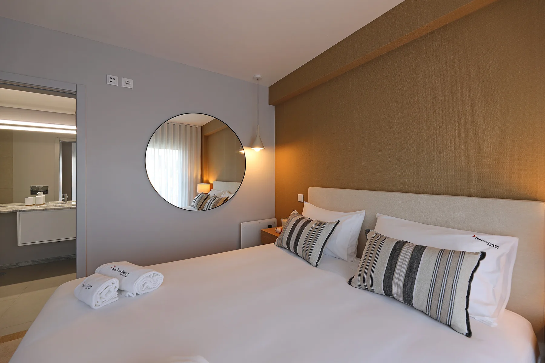 A bedroom with a neatly made bed and a round wall mirror.