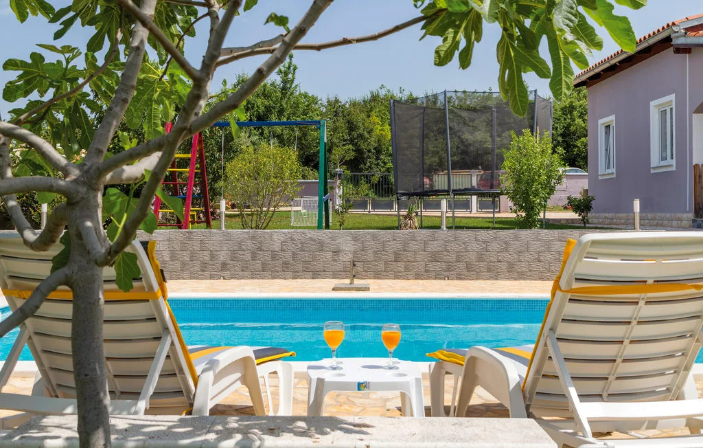 Una piscina con asientos de descanso da a un jardín y una zona de juegos.