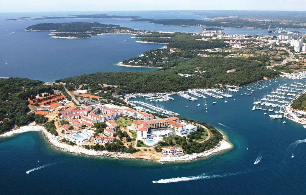 Vista aérea de una península turística junto a una marina y una costa boscosa.