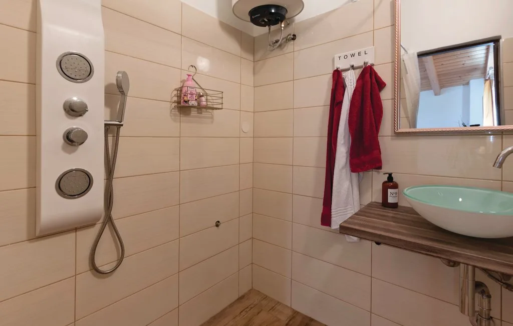 Un baño alicatado cuenta con una ducha de pared y un lavabo sobre una encimera de madera.