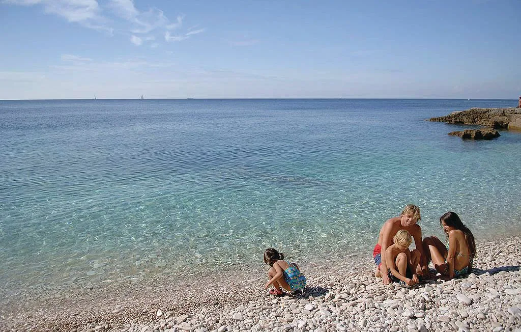 Una playa de piedras con personas sentadas junto al agua clara.