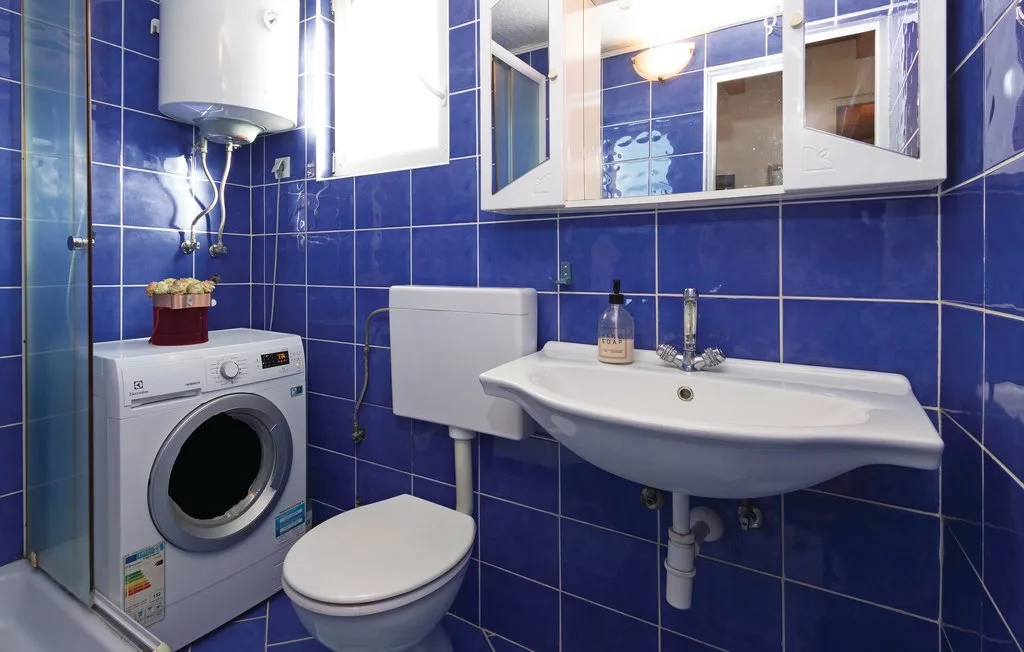 Un baño compacto con paredes de azulejos azules, lavabo, inodoro y lavadora.