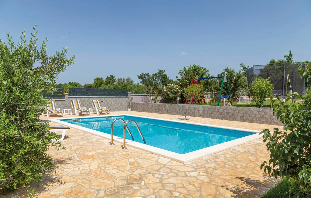 Una piscina al aire libre está rodeada por una terraza de piedra y asientos.