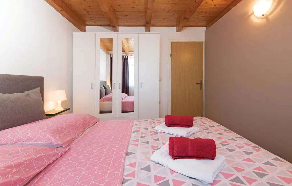 Un dormitorio con ropa de cama rosa estampada y un armario con espejo.