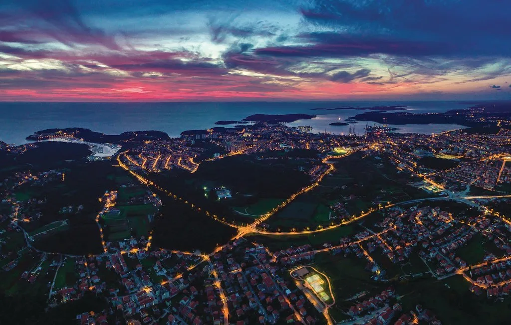 Vista aérea de una ciudad costera al anochecer, con caminos iluminados y bahías.