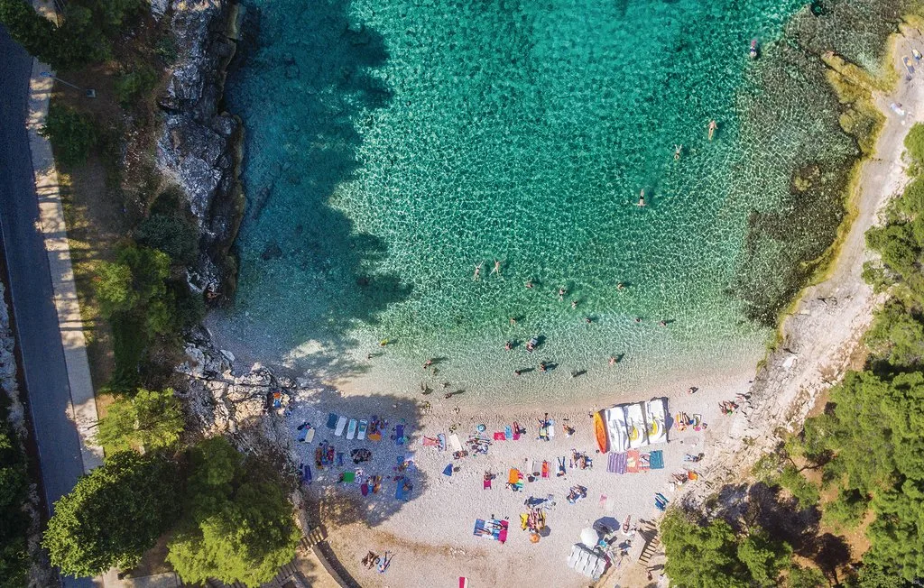 Vista aérea de una pequeña playa junto a aguas turquesas y transparentes.