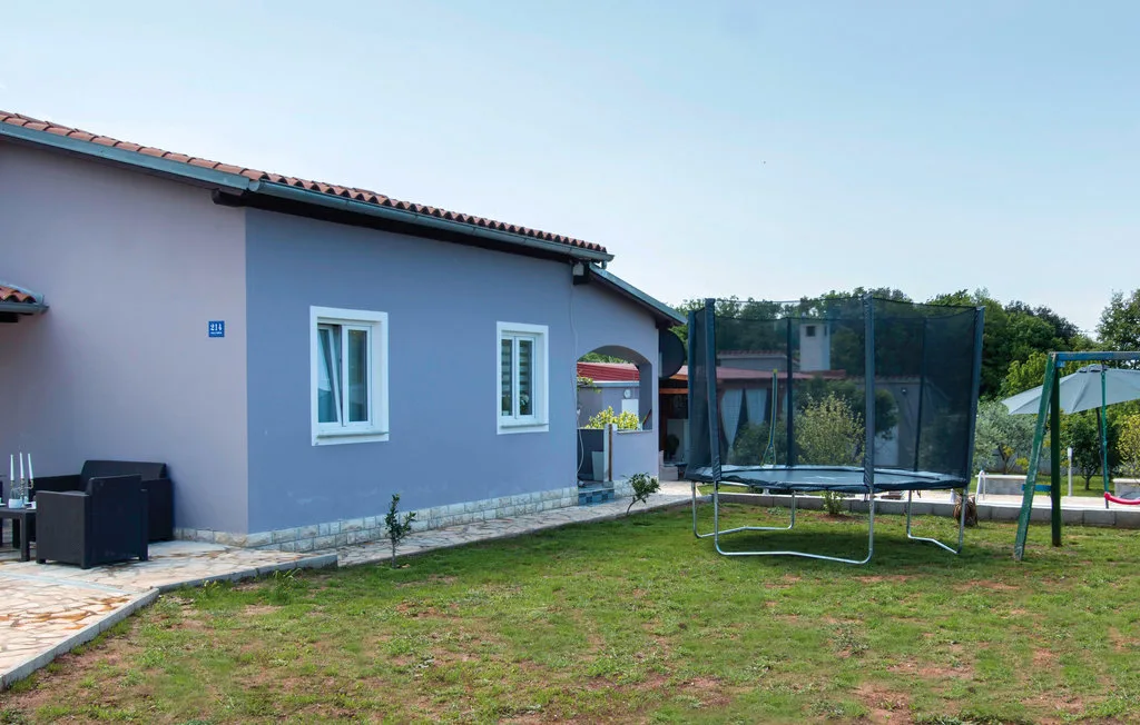 Una casa morada está junto a un patio con césped, un trampolín y un columpio.