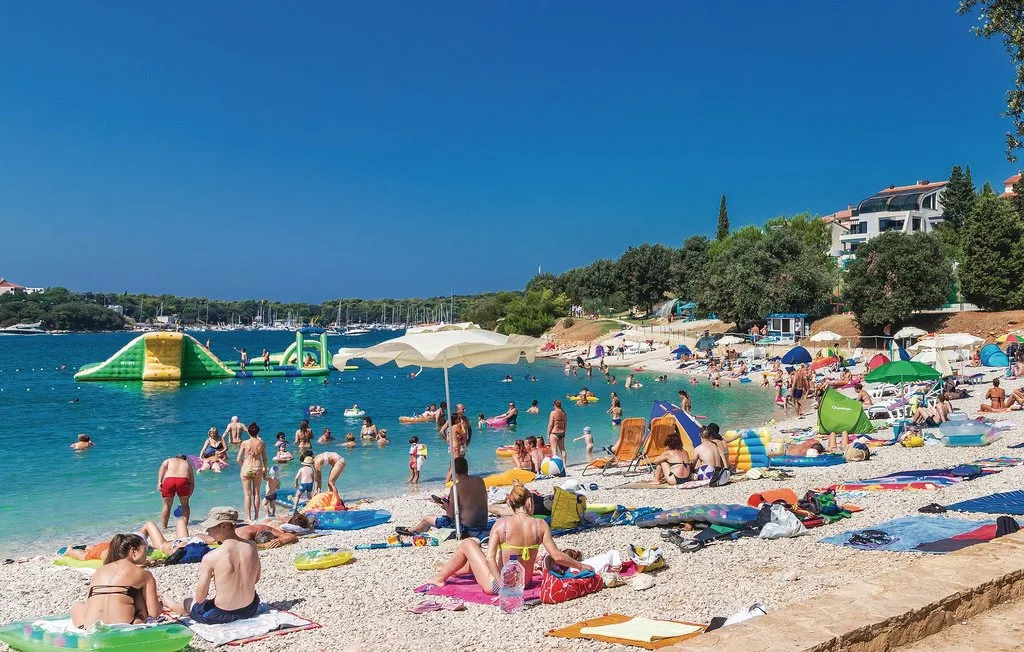 Una playa concurrida con bañistas, sombrillas y un circuito inflable en el agua.