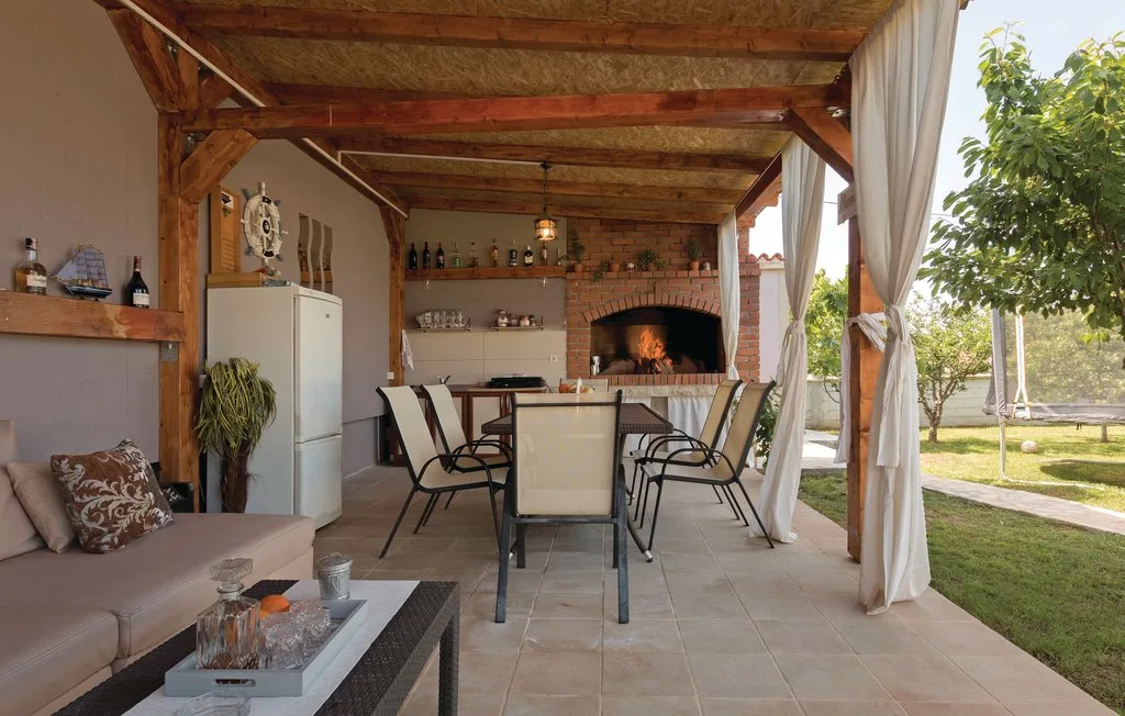 Comedor exterior cubierto con una mesa, asientos y una chimenea de ladrillo.