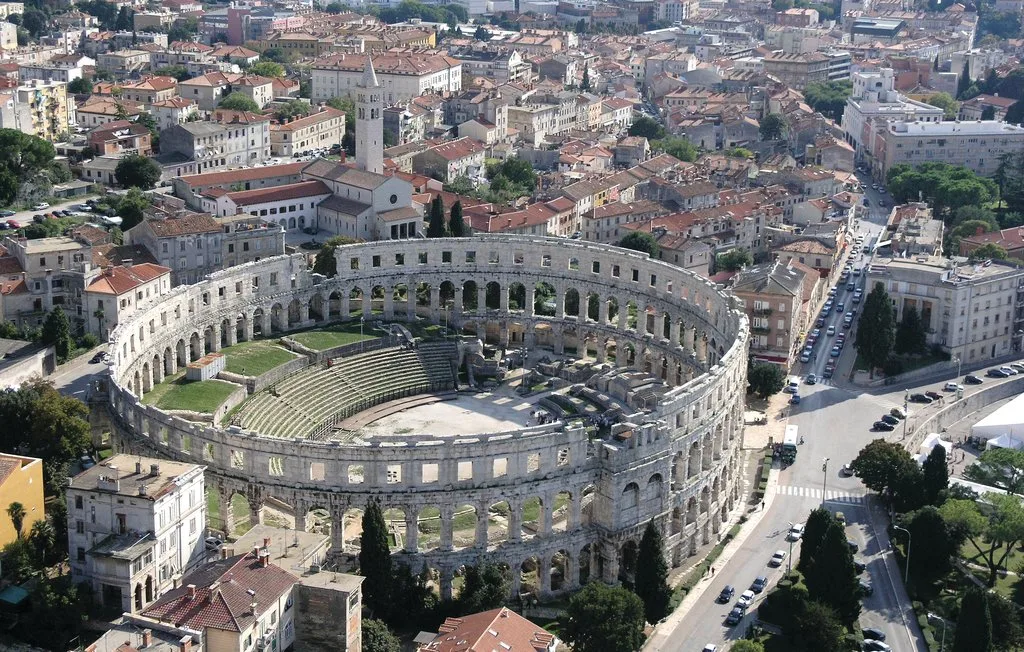 Un antiguo anfiteatro de piedra se alza entre edificios urbanos.