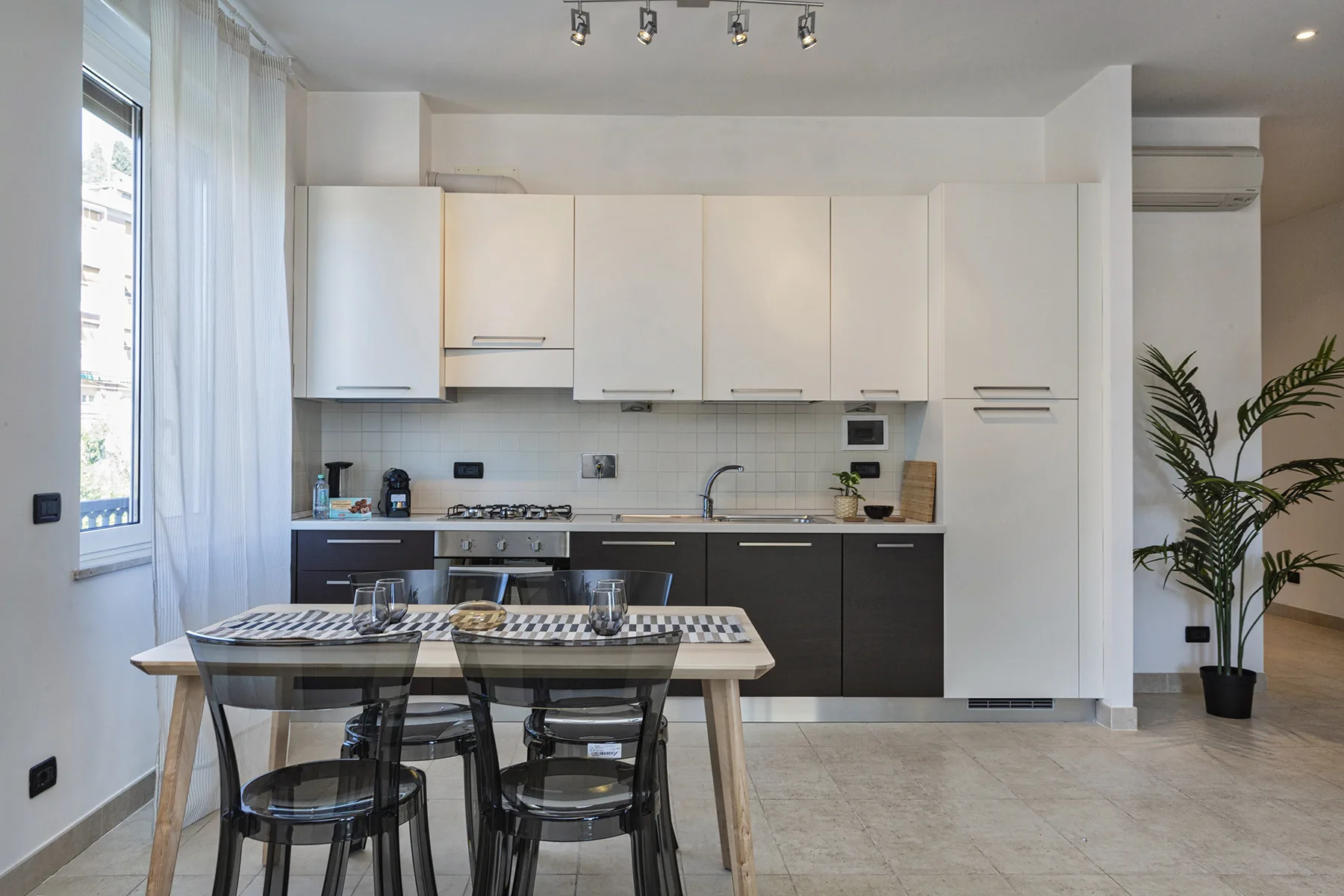 Una cocina y comedor luminosos con gabinetes blancos y una mesa junto a la ventana.