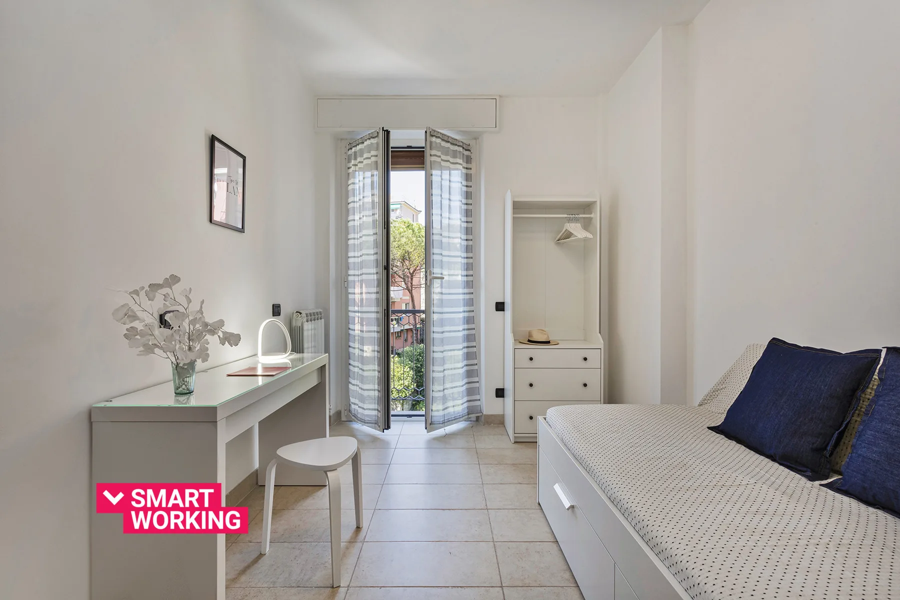 Un dormitorio luminoso con una cama, un escritorio y puertas abiertas al balcón.
