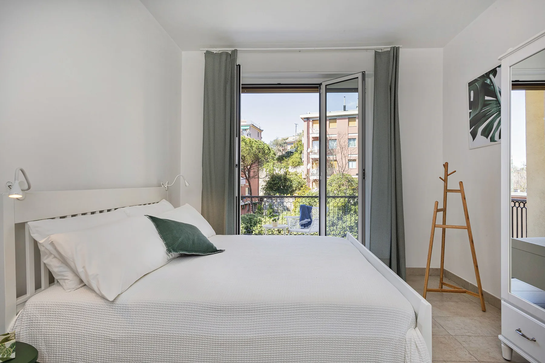 Un dormitorio luminoso con una cama tendida y la puerta del balcón abierta.