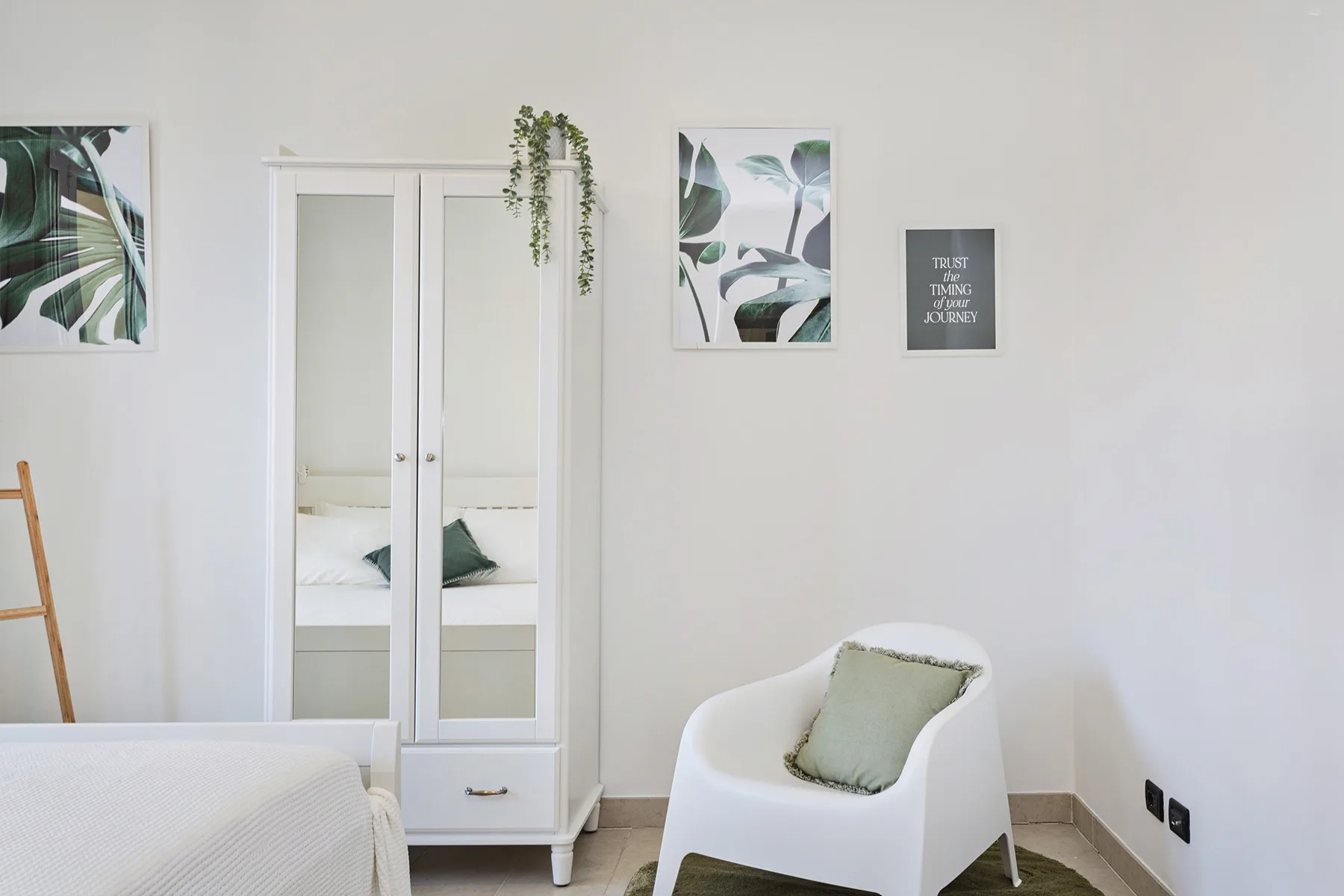 Un dormitorio luminoso con una cama blanca, un armario con espejo y una silla tapizada.