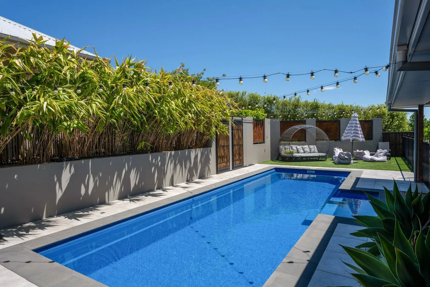 Zona de descanso junto a la piscina con jardines y guirnaldas de luces.
