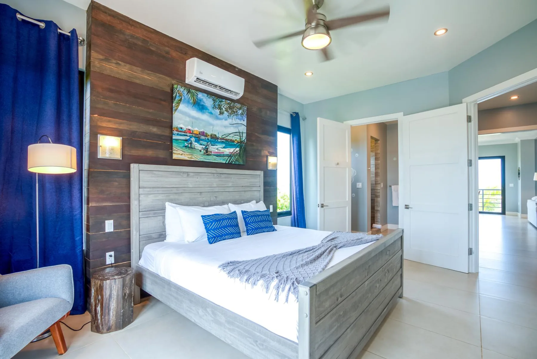 A bright bedroom with a large bed, blue curtains, and a ceiling fan.