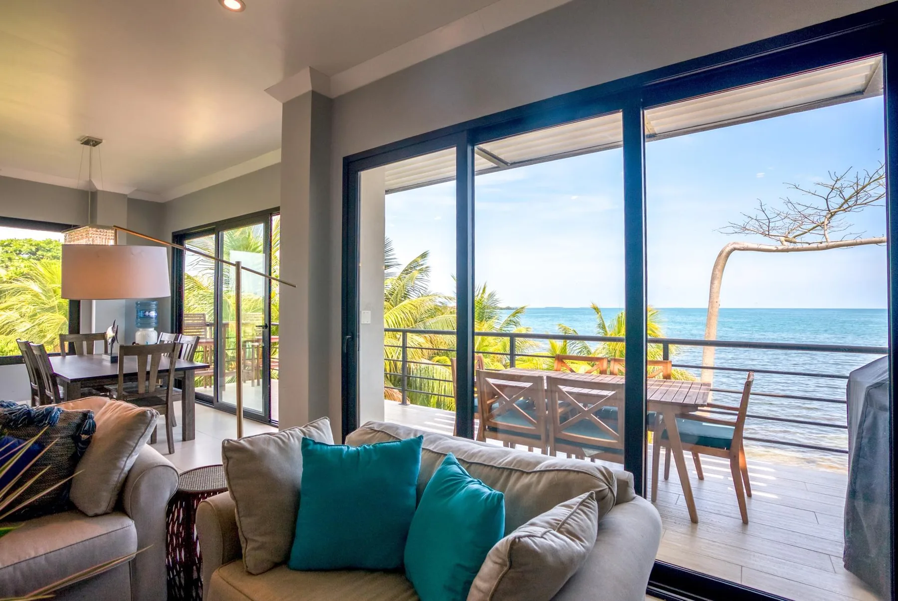 A living area opens onto a deck with outdoor seating and an ocean view.