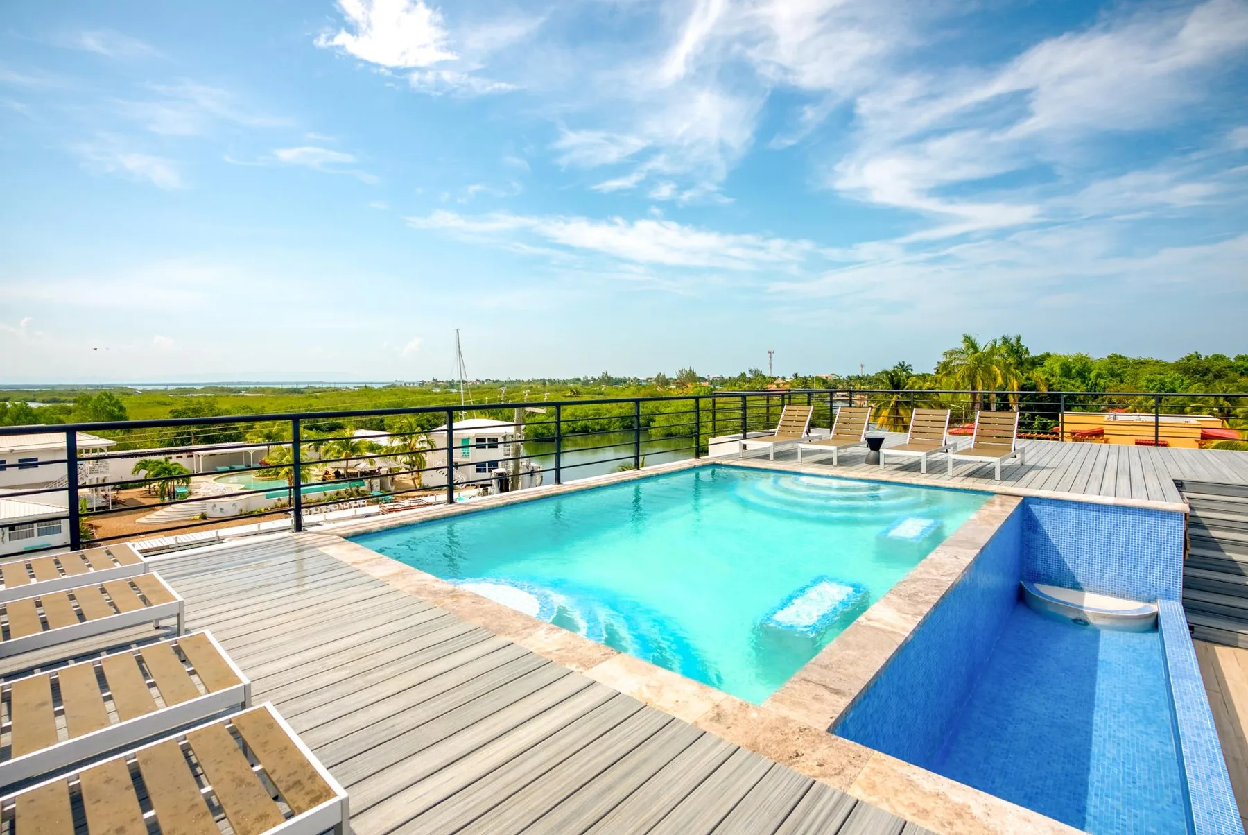 A rooftop pool sits beside a wooden deck with lounge chairs and a wide sky view.