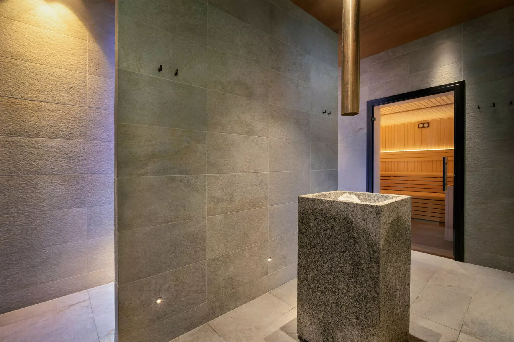 A tiled spa room with a stone basin and a wooden sauna visible through the doorway.