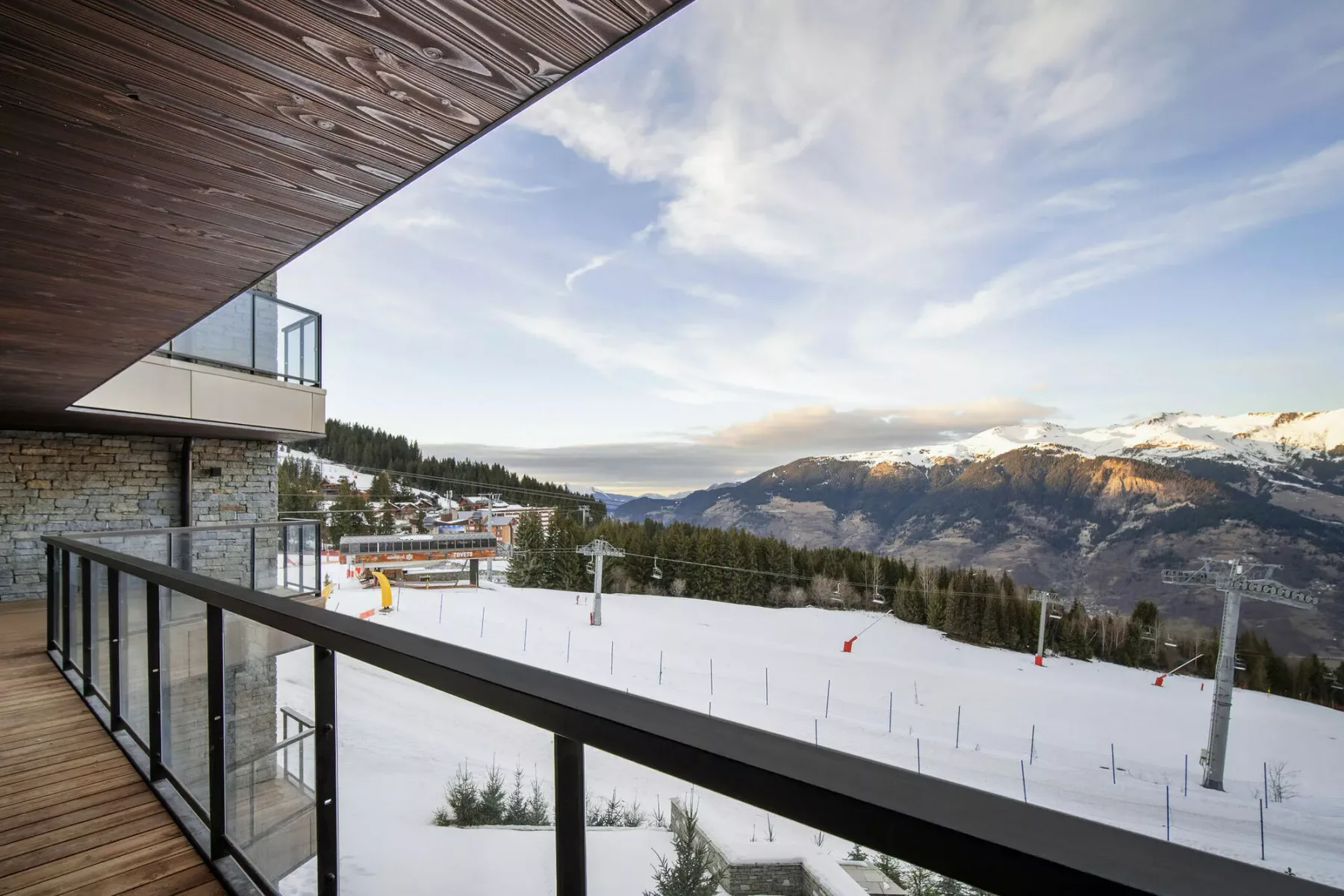 A balcony overlooks a snowy ski slope and mountain range.