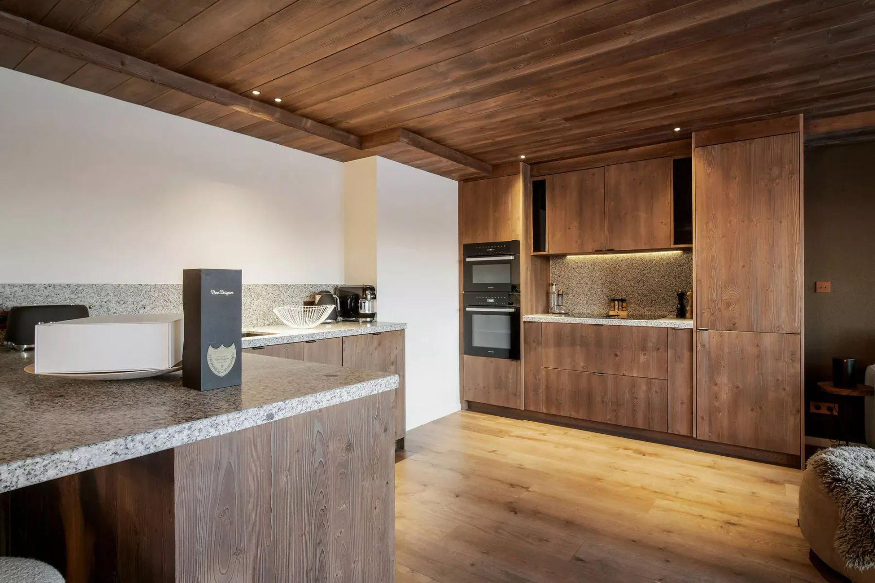 A modern kitchen with wooden cabinetry, stone countertops, and a central island.