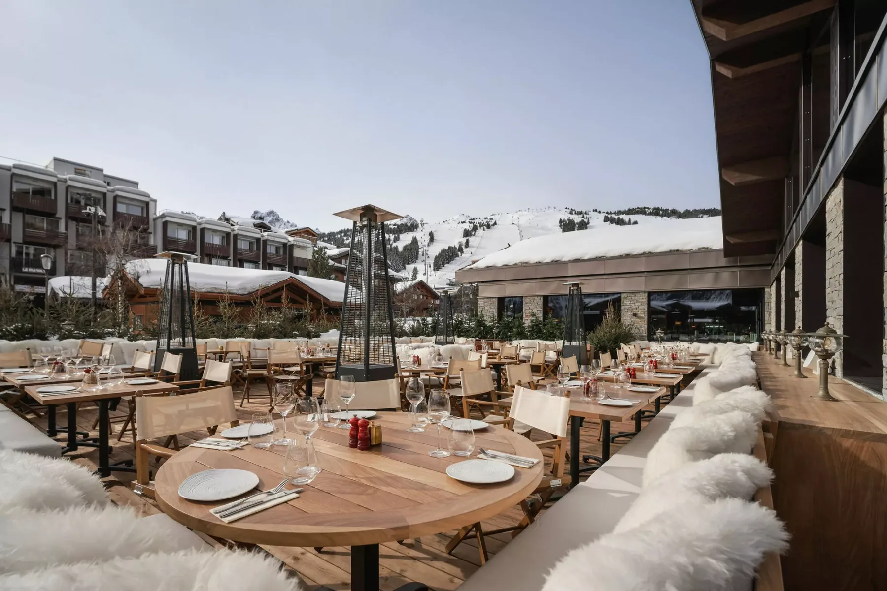An outdoor dining terrace with set tables and snowy mountains in the background.