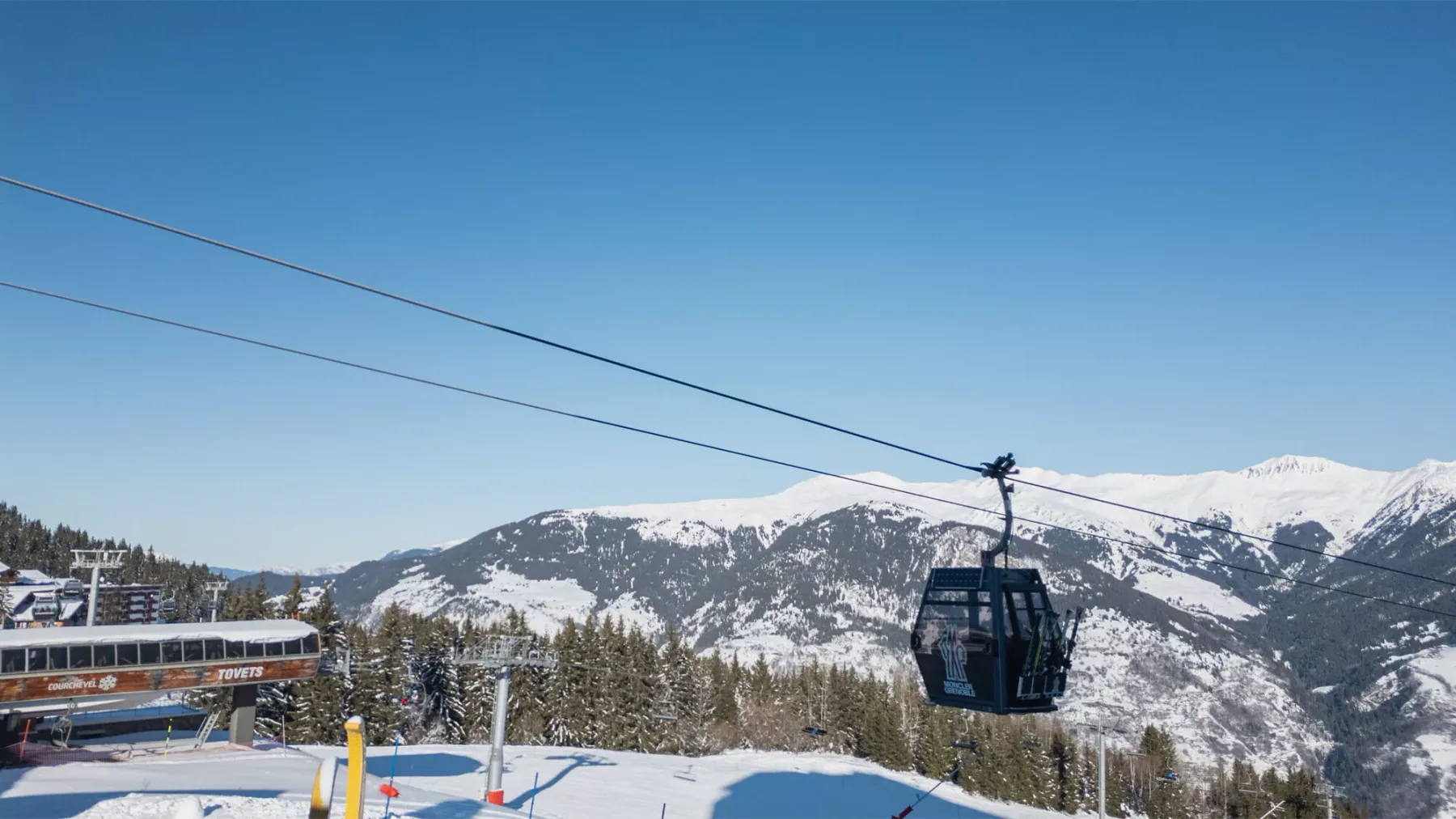 A gondola cabin travels above a snowy mountain landscape.