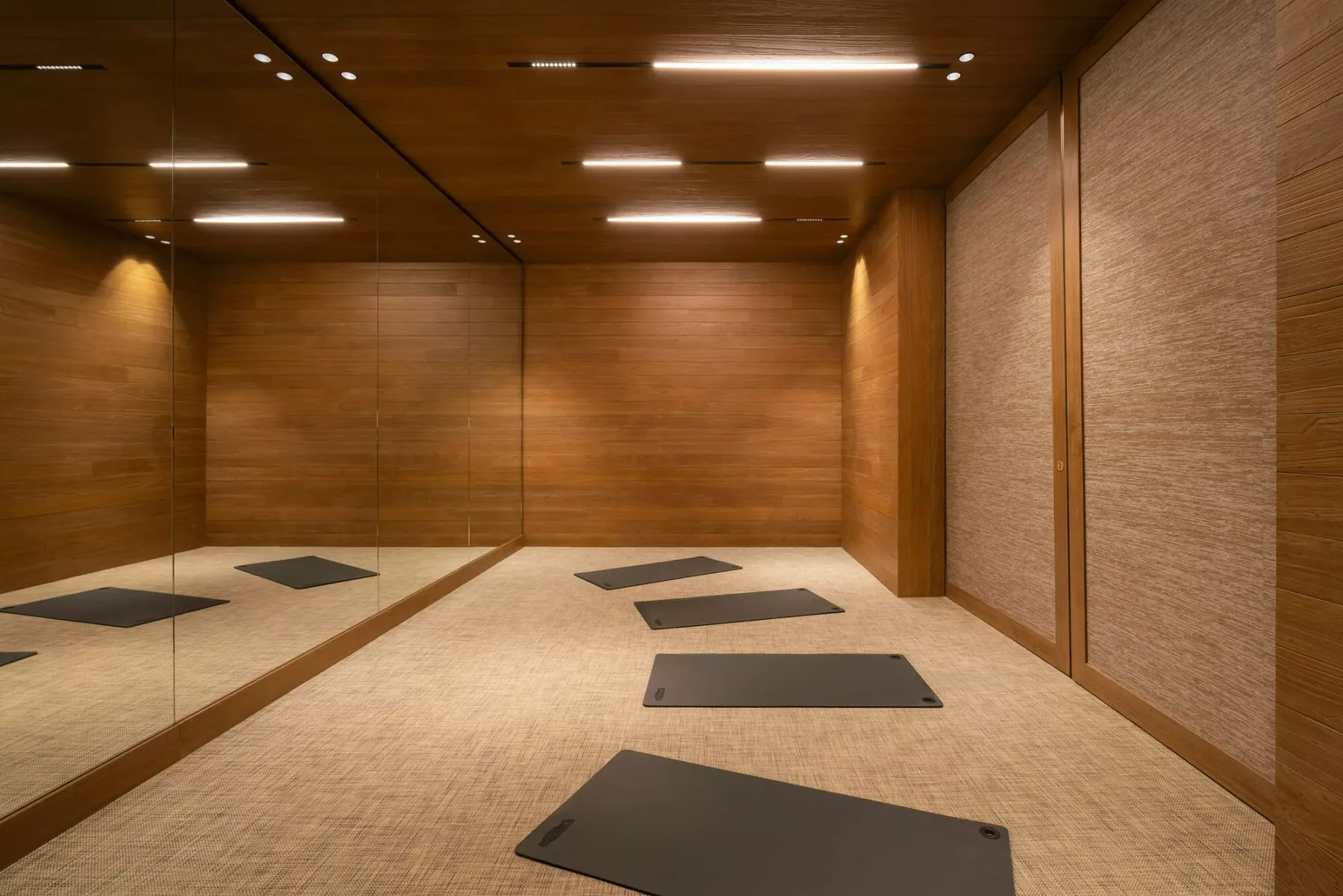 A warm-toned exercise room with floor mats and a mirrored wall.