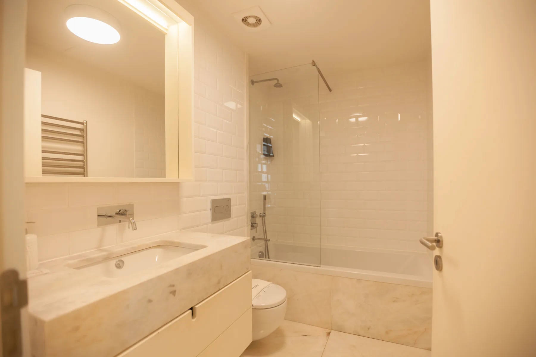 Baño con lavabo, espejo y bañera detrás de una mampara de vidrio.
