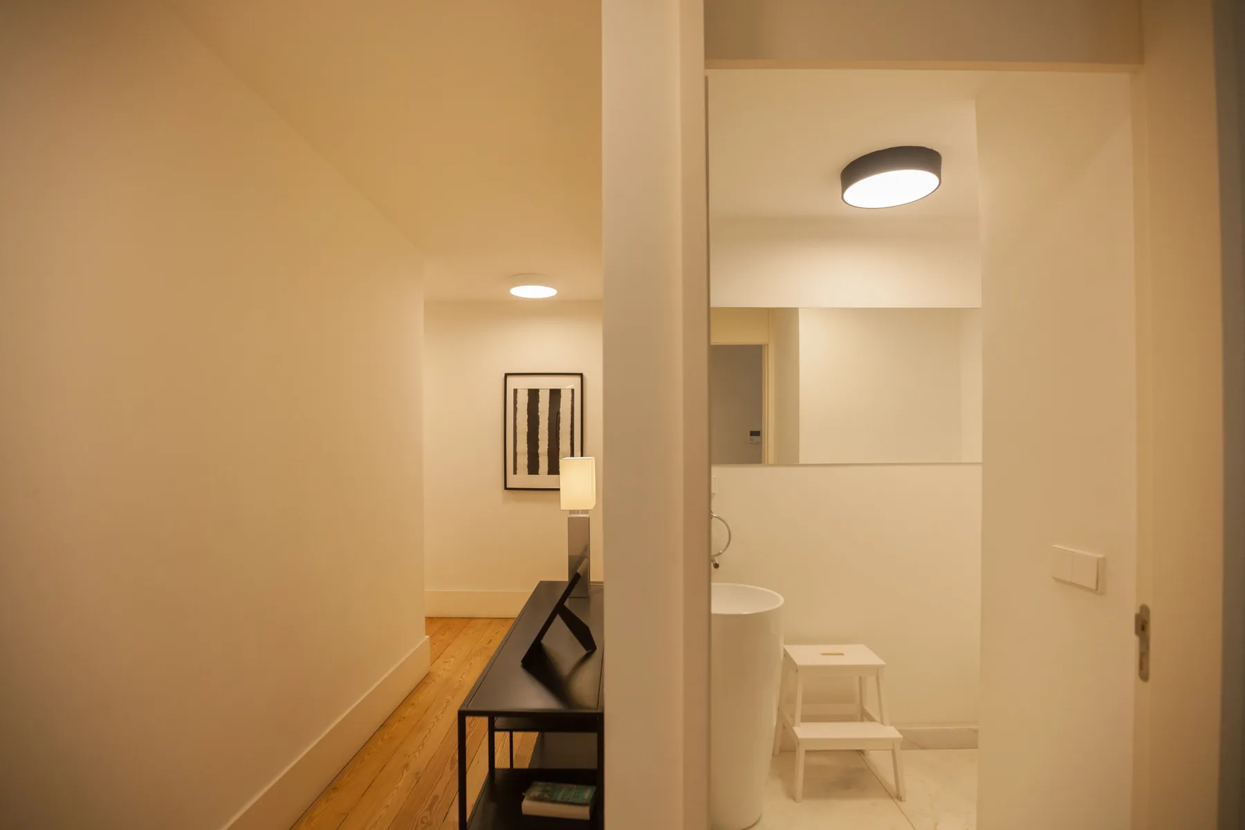 Un pasillo da a un baño con lavabo y un pequeño taburete.