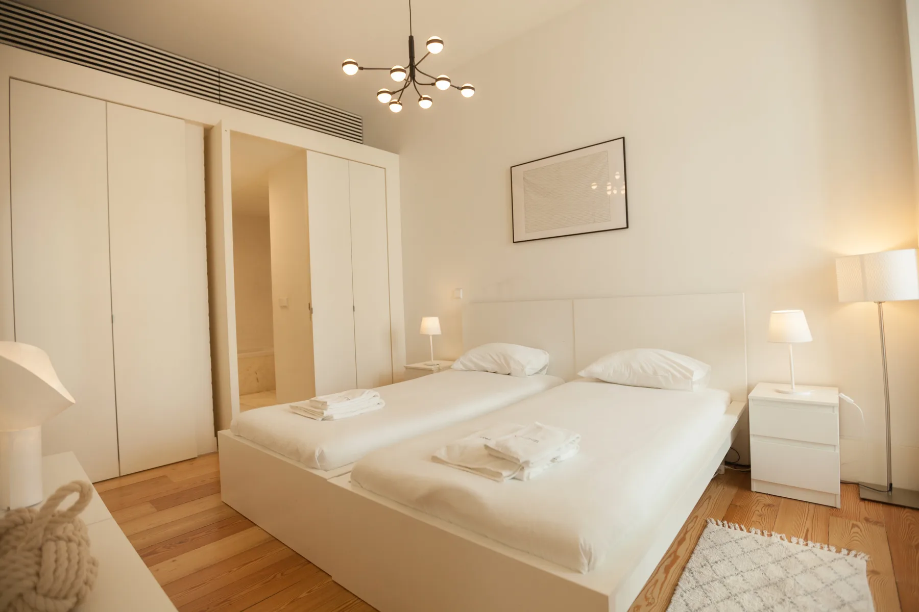 Un dormitorio luminoso con dos camas, mesillas y una lámpara de techo.