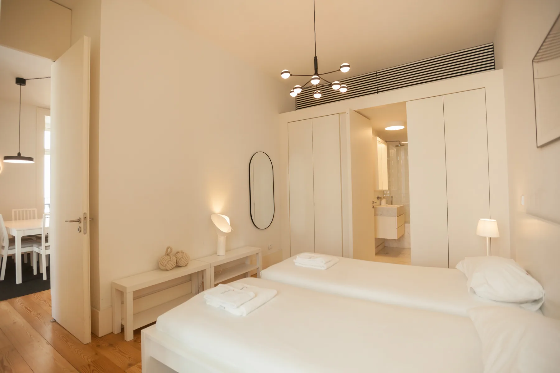 Un dormitorio luminoso con dos camas y una puerta hacia el baño.
