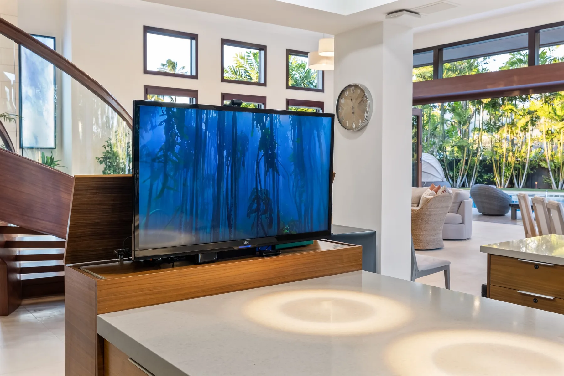 Una luminosa sala de estar tiene un televisor grande junto a una escalera y una zona de asientos abierta.