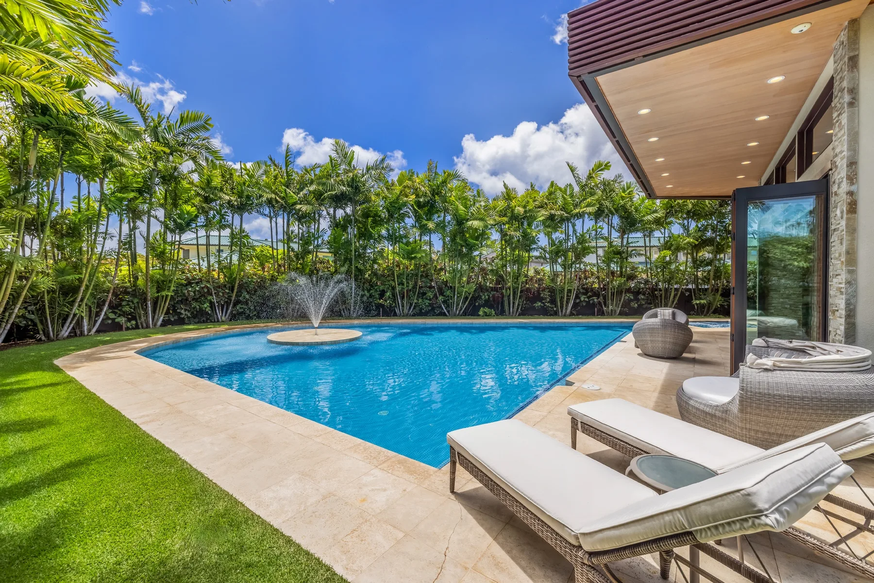 Piscina al aire libre junto a un patio con asientos y vegetación tropical.