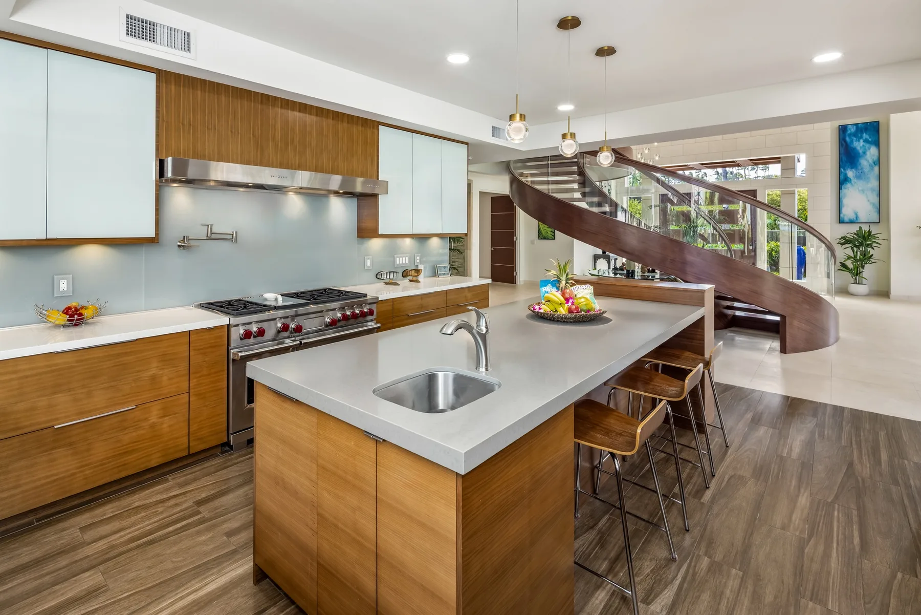 Una cocina moderna con una isla grande y una escalera curva al fondo.