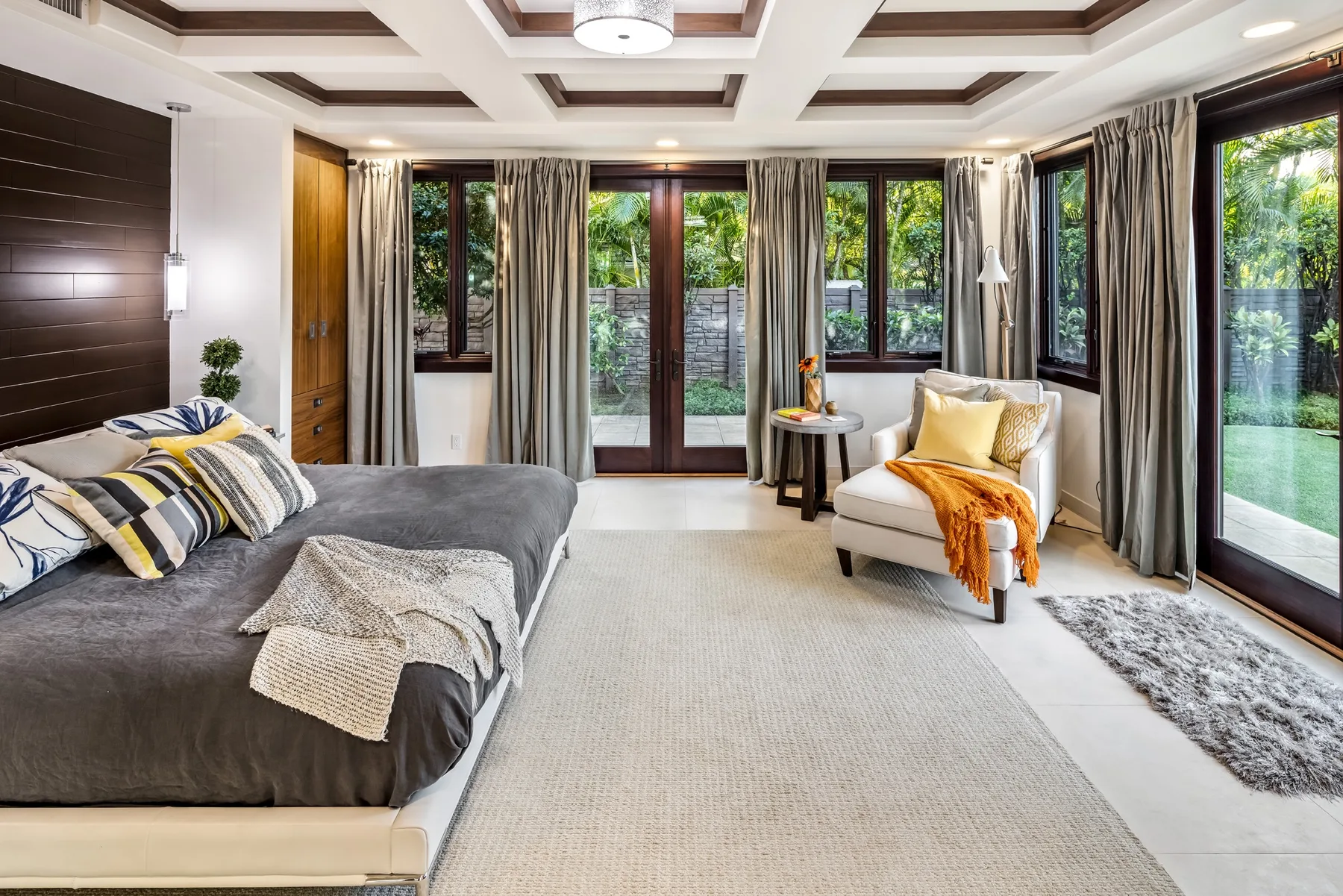 Un dormitorio luminoso con una cama grande, un sillón y ventanas con vistas a la vegetación.