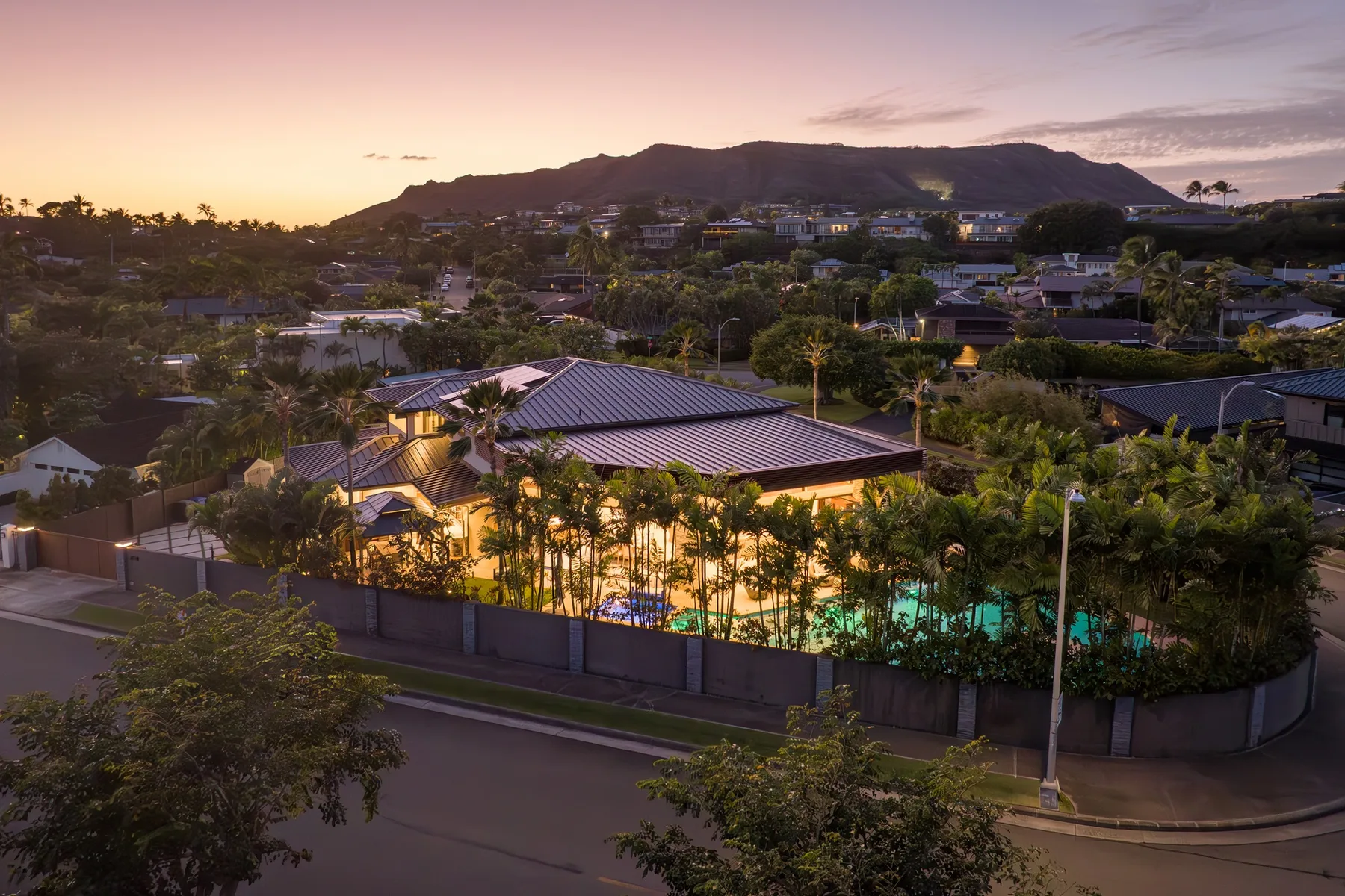 Una piscina exterior iluminada y edificios cercanos se encuentran bajo una montaña al atardecer.