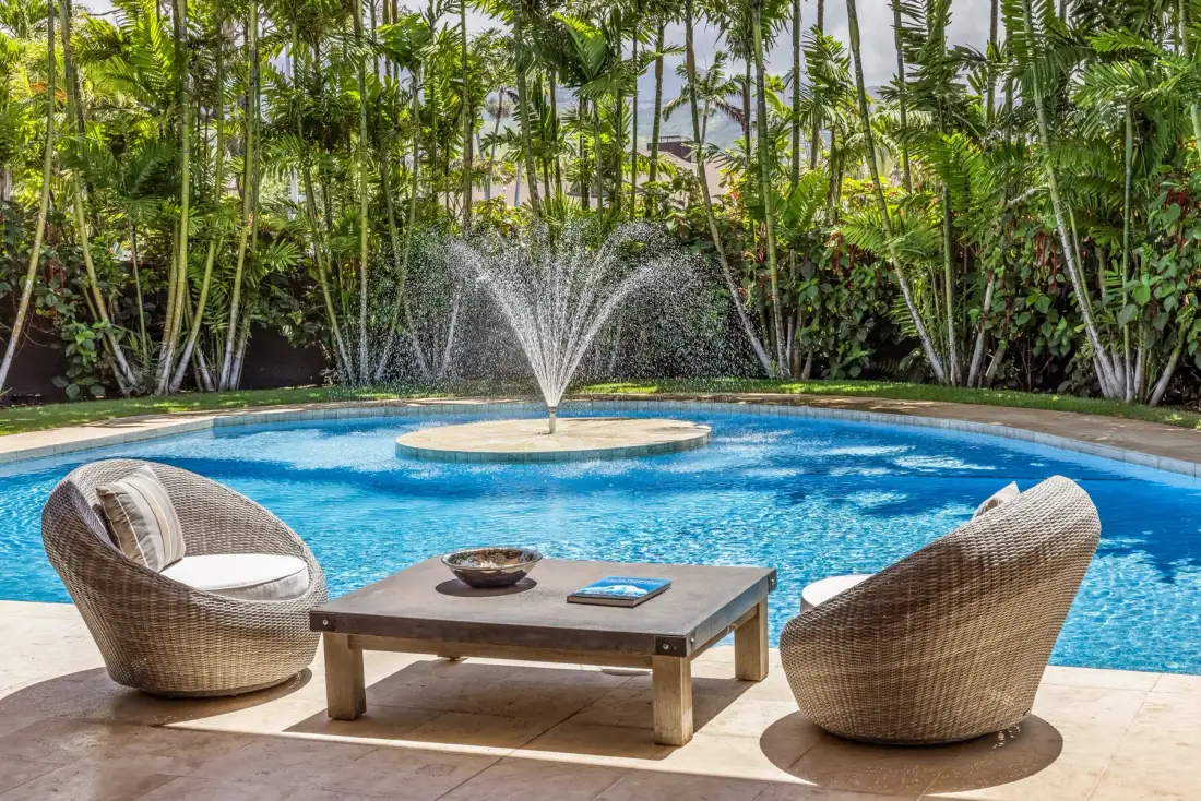 Una piscina con una fuente central y dos asientos junto al patio.