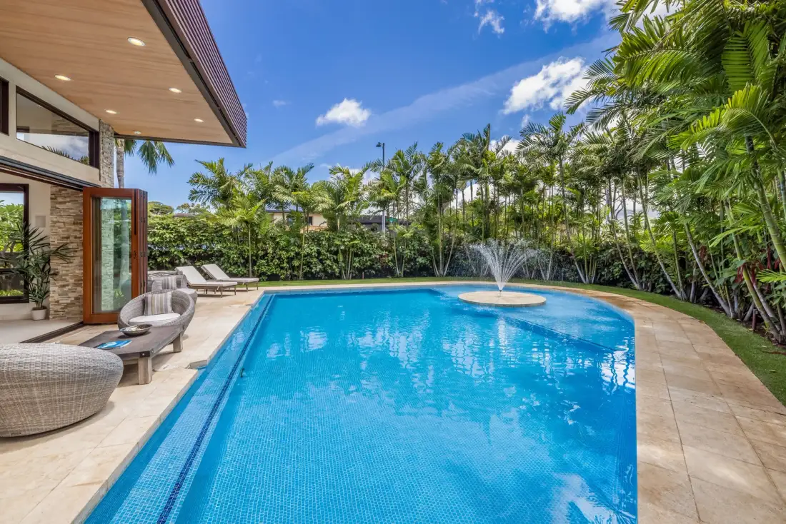 Una piscina al aire libre con una fuente, rodeada de vegetación tropical.