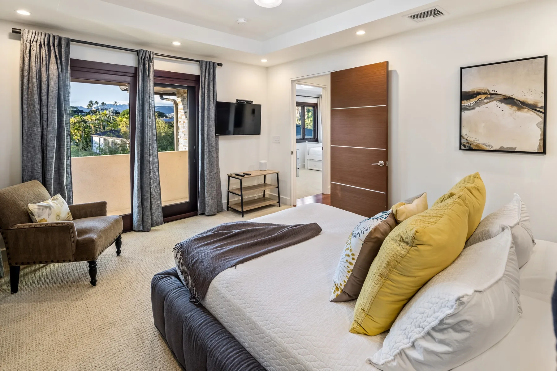 Un dormitorio con una cama, un sillón y ventanas altas con cortinas.