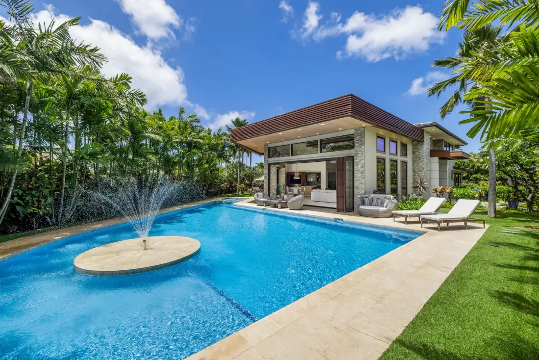 Una casa moderna junto a una piscina, con tumbonas en el patio.