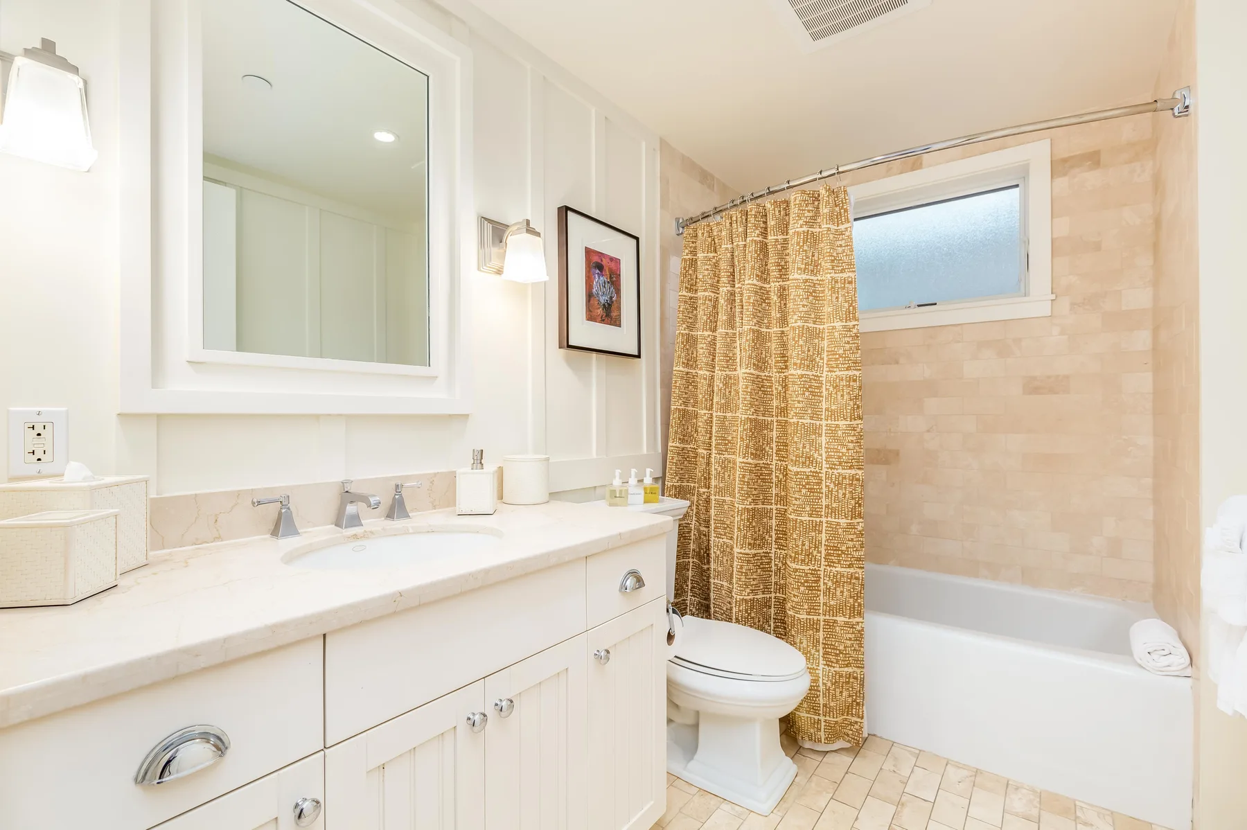 A bright bathroom with a sink vanity, toilet, and curtained bathtub.