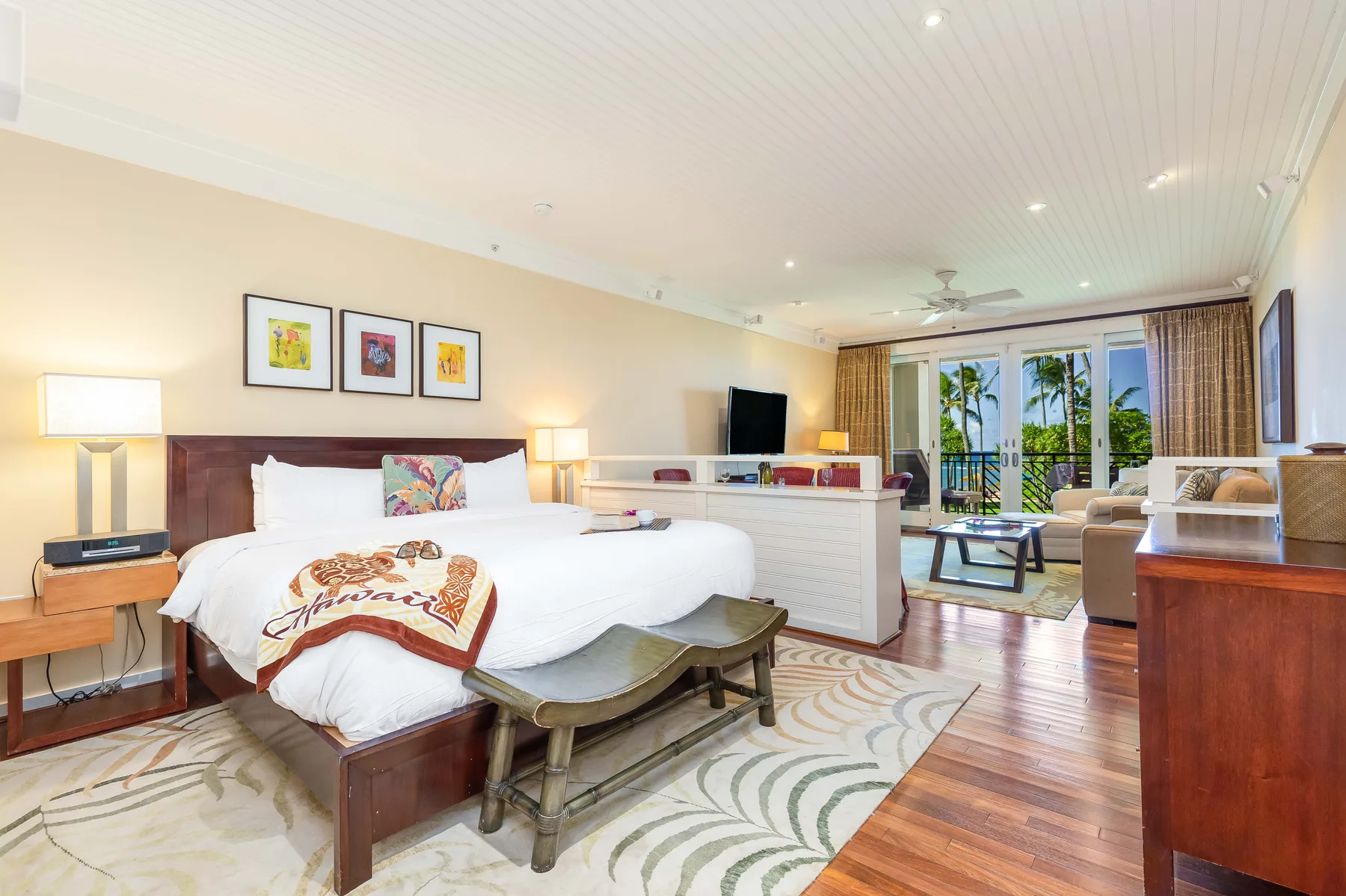 A bright bedroom with a large bed, a desk, and glass doors opening to a balcony.