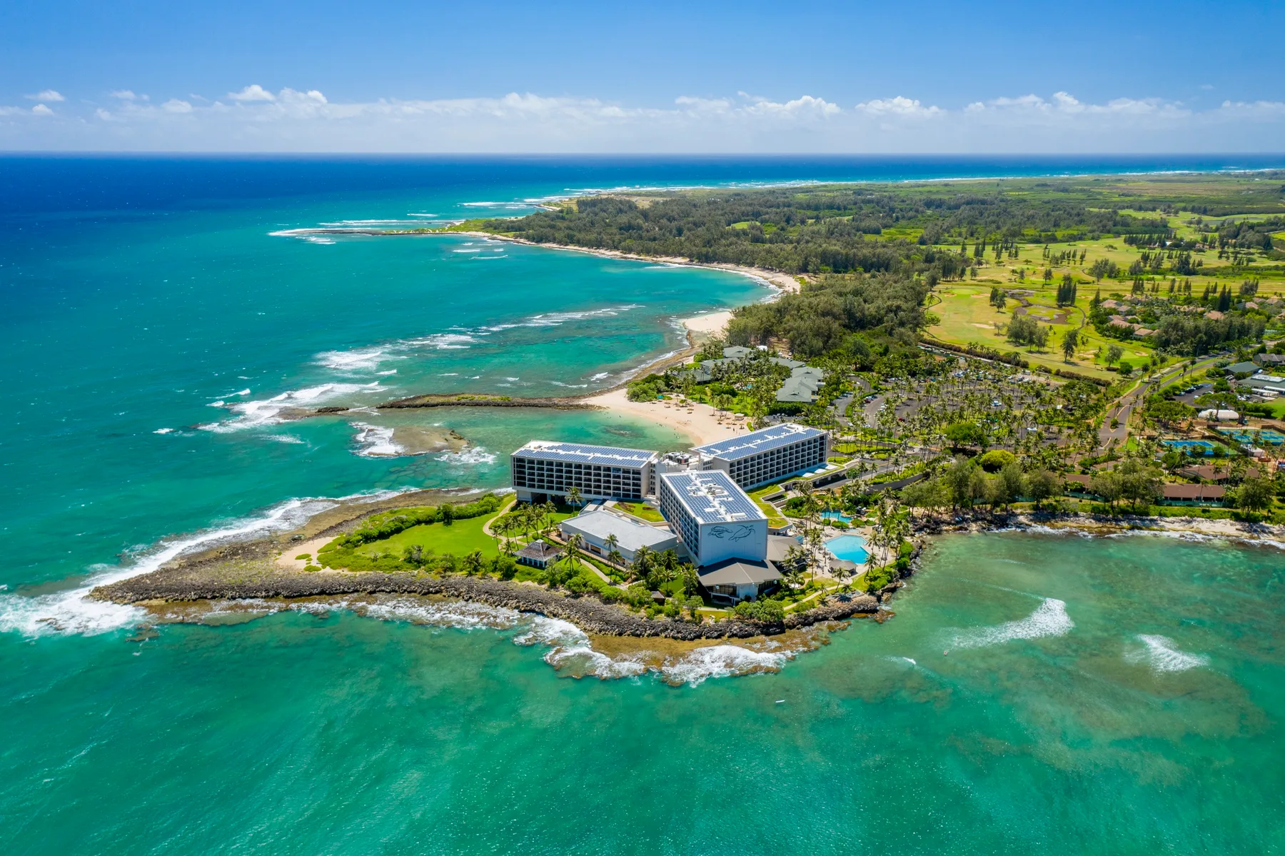 Aerial view of a coastal resort beside turquoise ocean water and green shoreline.