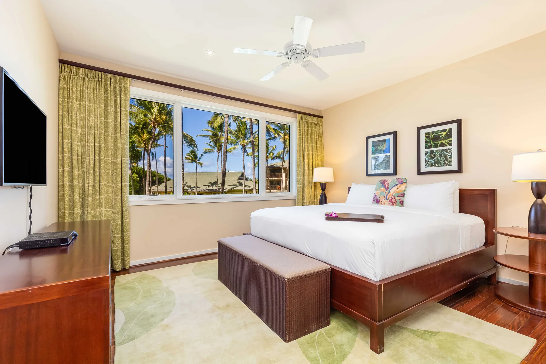 A bright bedroom with a large bed and windows overlooking palm trees.