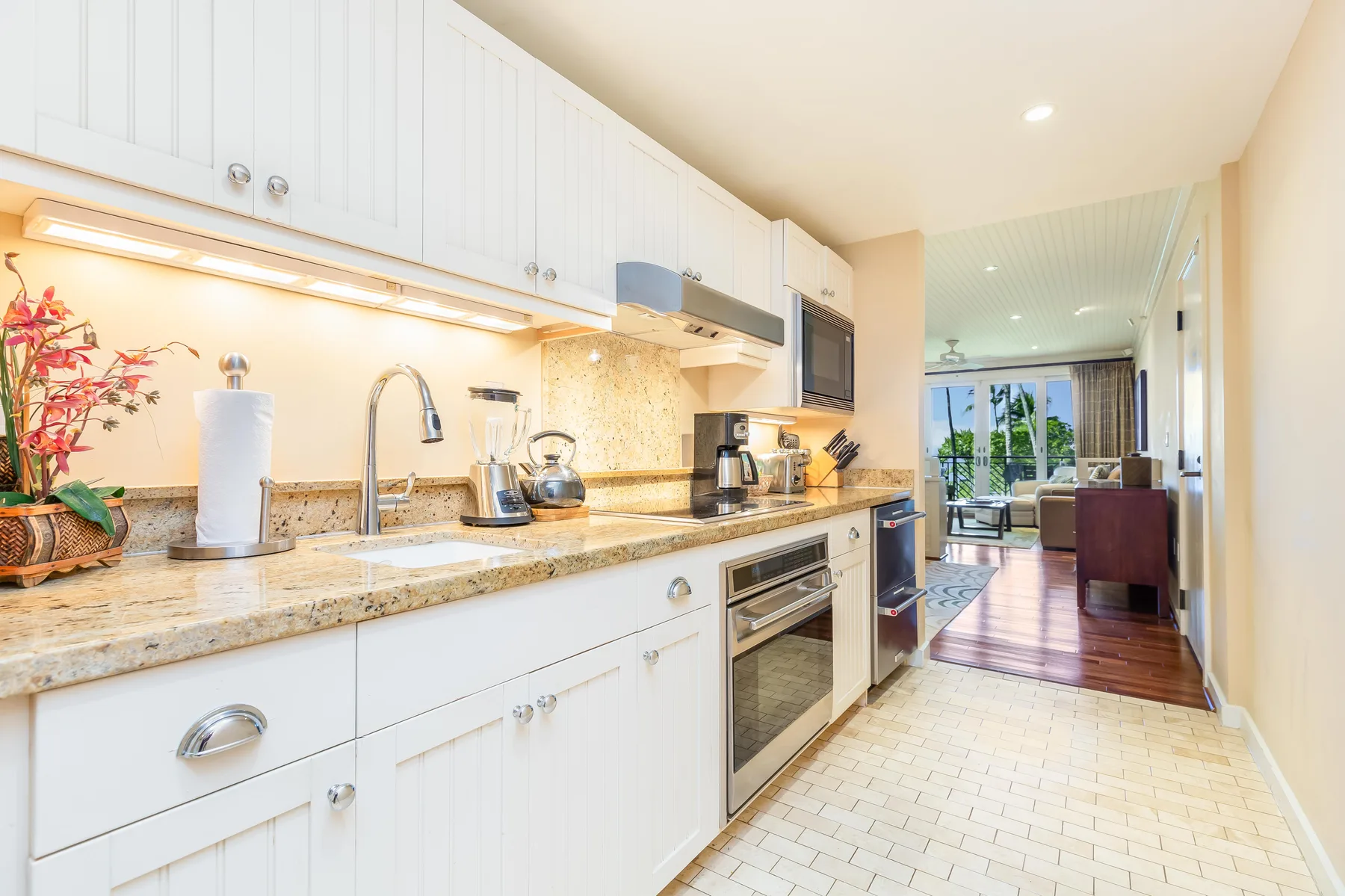 A bright kitchen with white cabinets and a long countertop opening onto a living area.