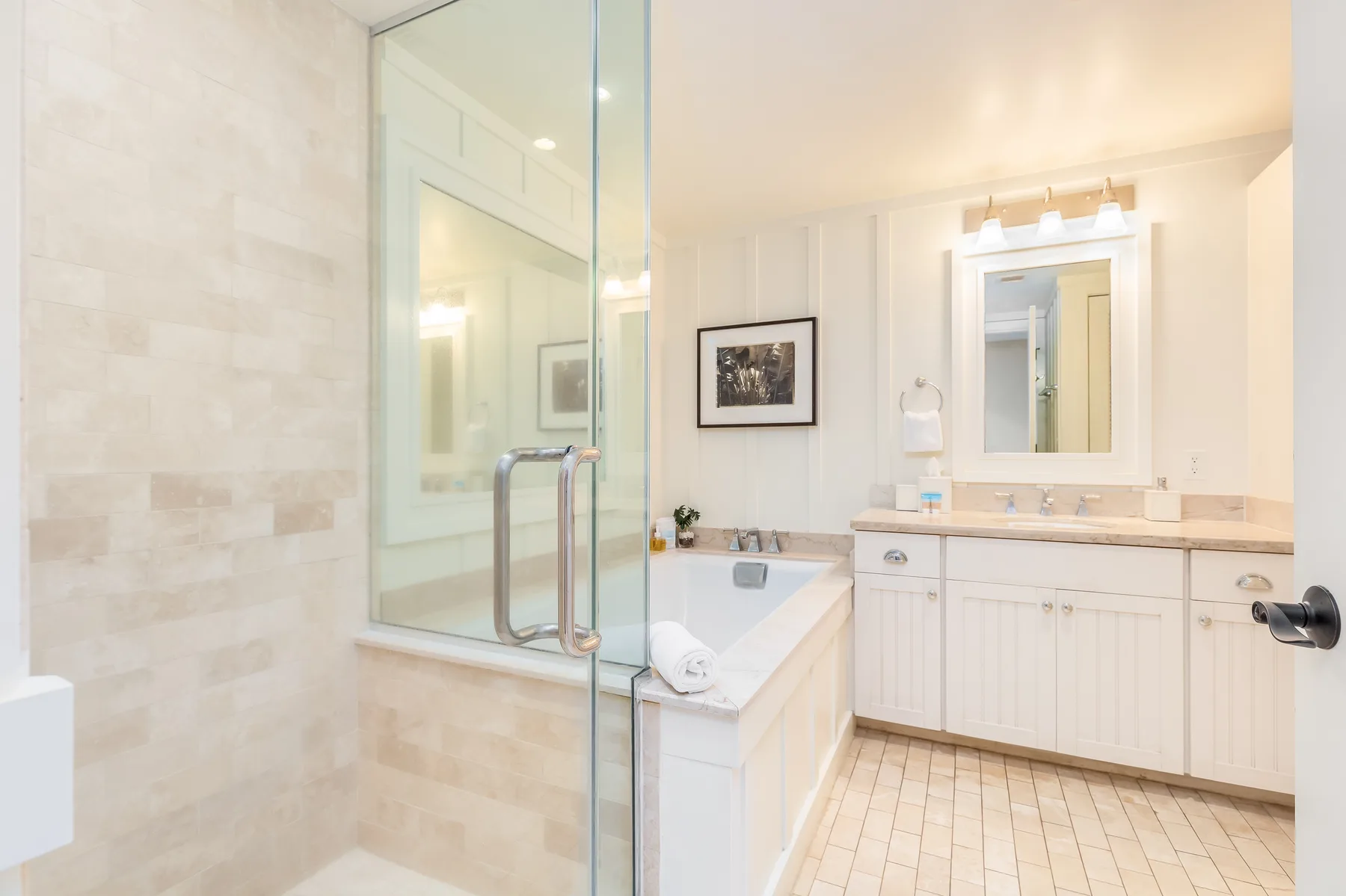 A bright bathroom with a glass shower, bathtub, and vanity.