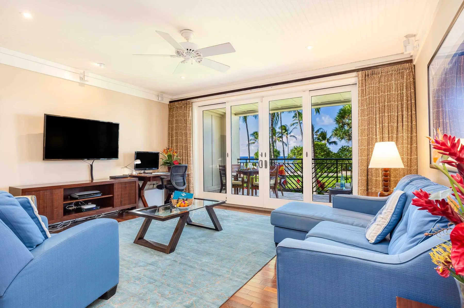 A bright living room with blue seating, a television, and glass doors opening to a balcony.