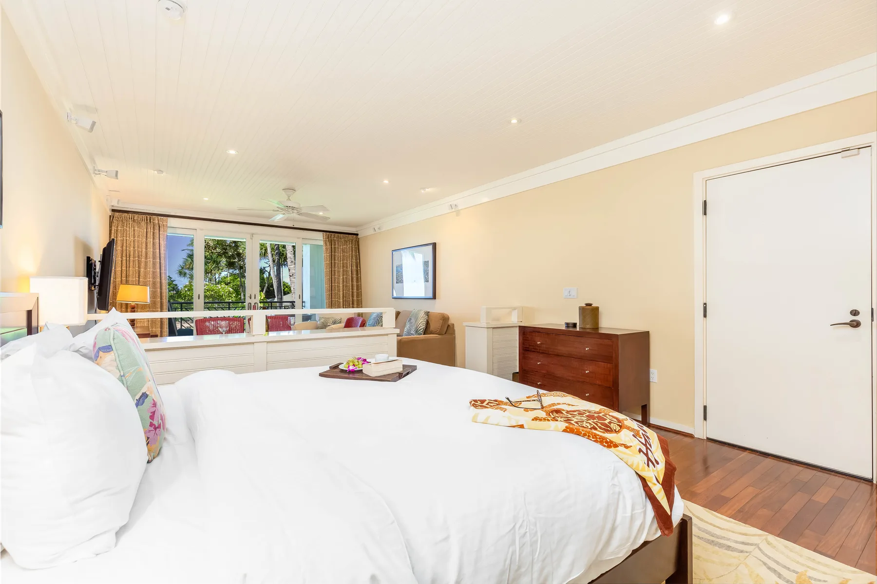 A bedroom with a large bed, a dresser, and windows overlooking greenery.