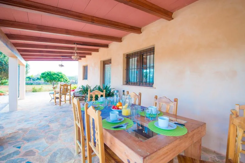 A covered dining area with a wooden table set with colorful dishes and glasses.